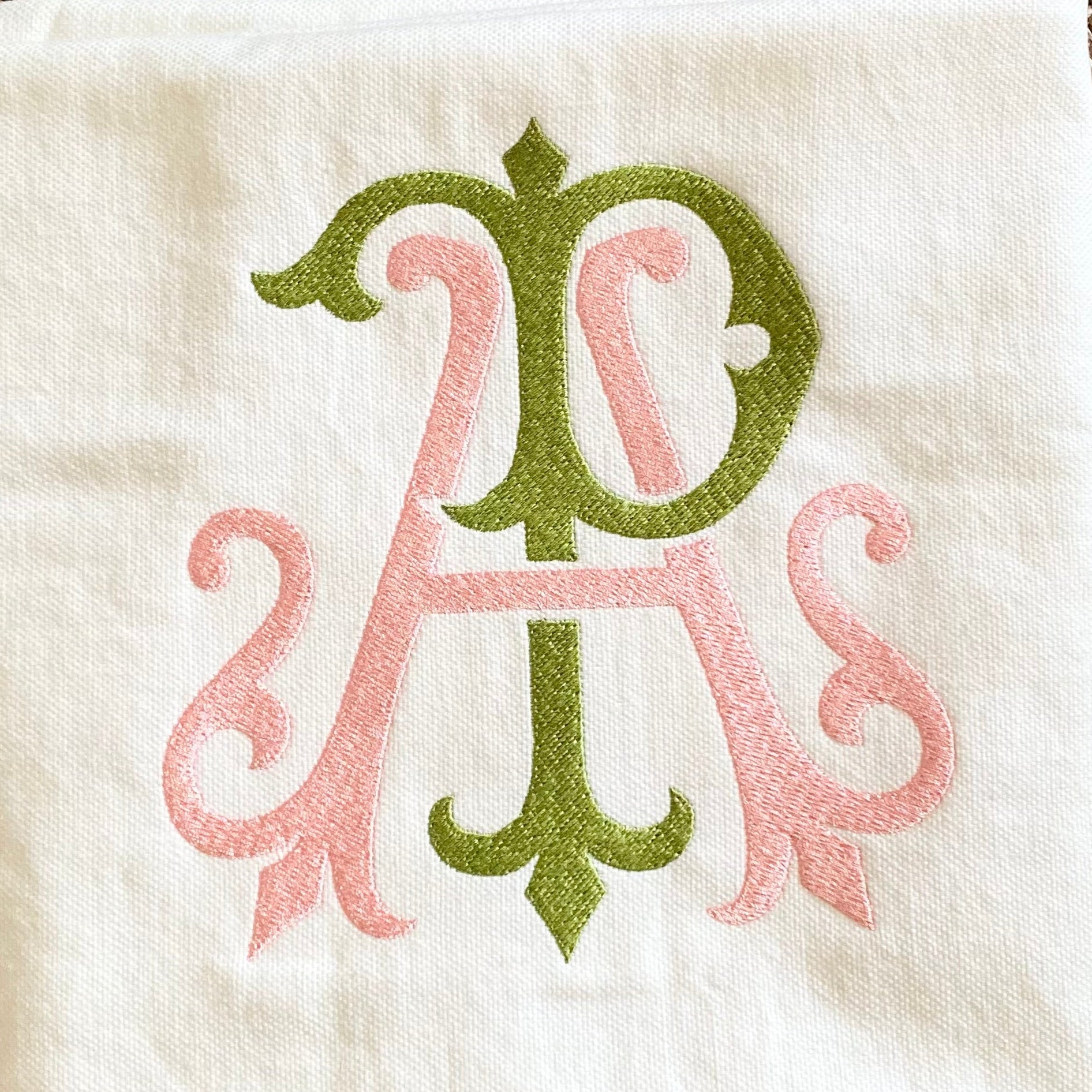 Folded white towel with pink and green monogram on a textured brown surface